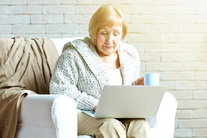 Older woman sitting on couch on laptop with a cup of coffee